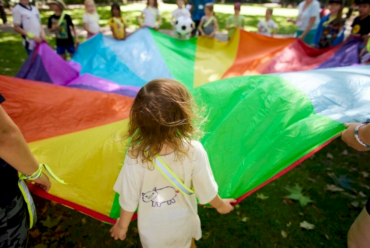 A group of children are playing with a colourful parachute.