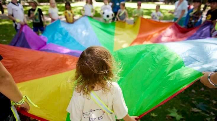 A group of children are playing with a colourful parachute.